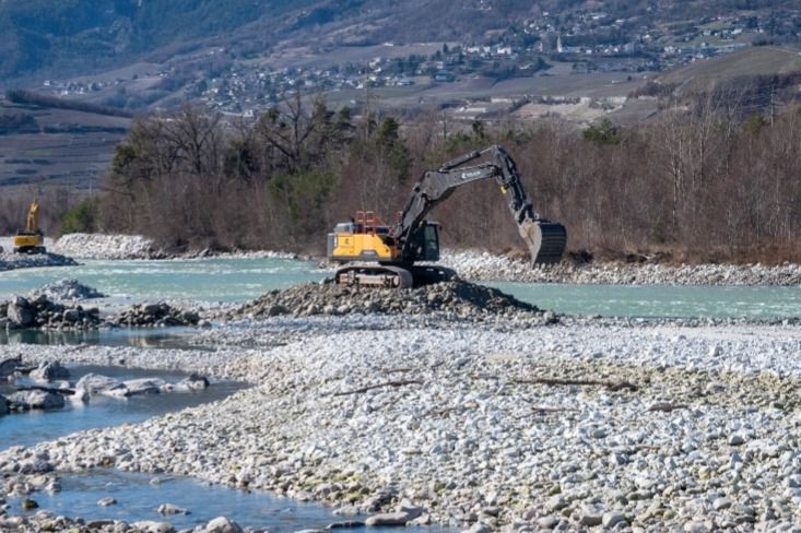 Blick auf einen kleinen Fluss mit Kiesbank, wo Menschen spielen und entspannen, der Fluss ist von Bäumen umgeben.